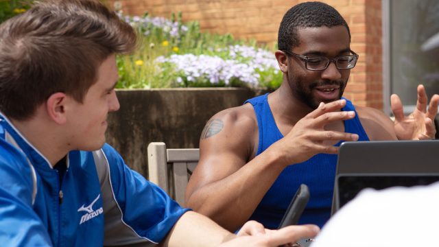 Two students sitting outside with laptops