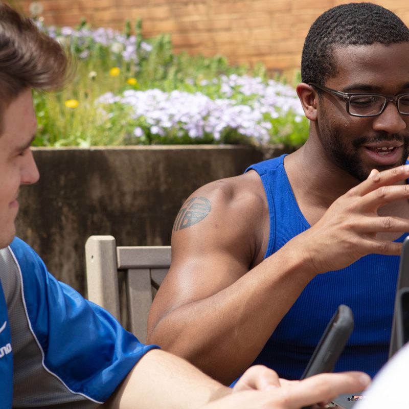 Two students sitting outside with laptops