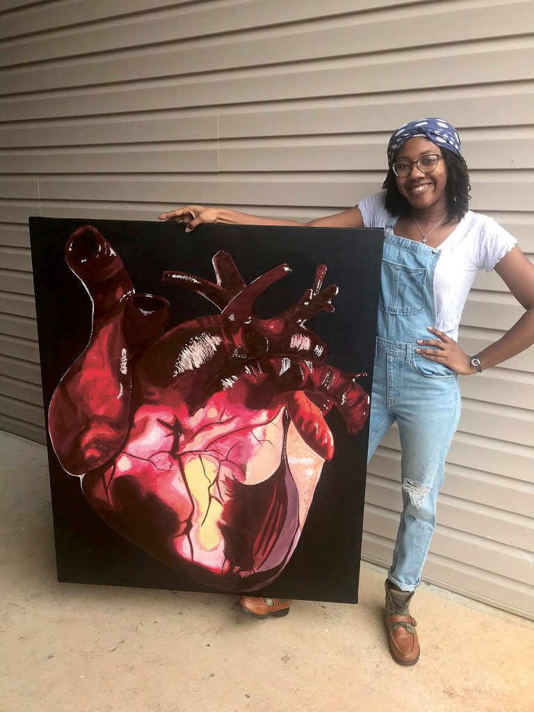 Young woman stands next to a painting of a human heart