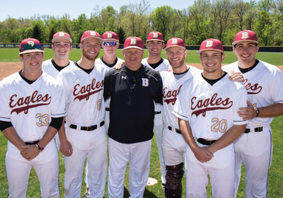 College baseball players stand on either side of their coach on the field||