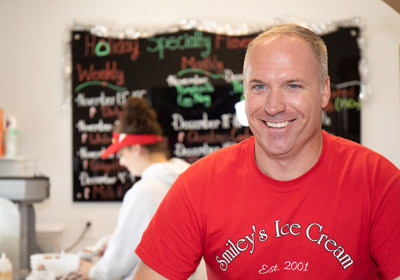 Man in red shirt smiling in foreground Young woman in background scooping ice cream