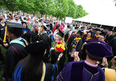 young woman holding flowers wearing a cap and gown in a crows of people||||||||||||||||