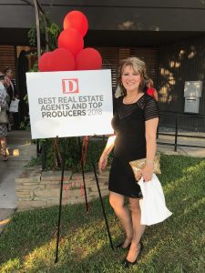 Woman stands next to sign that says Best Real Estate Agents and Top Producers 2018