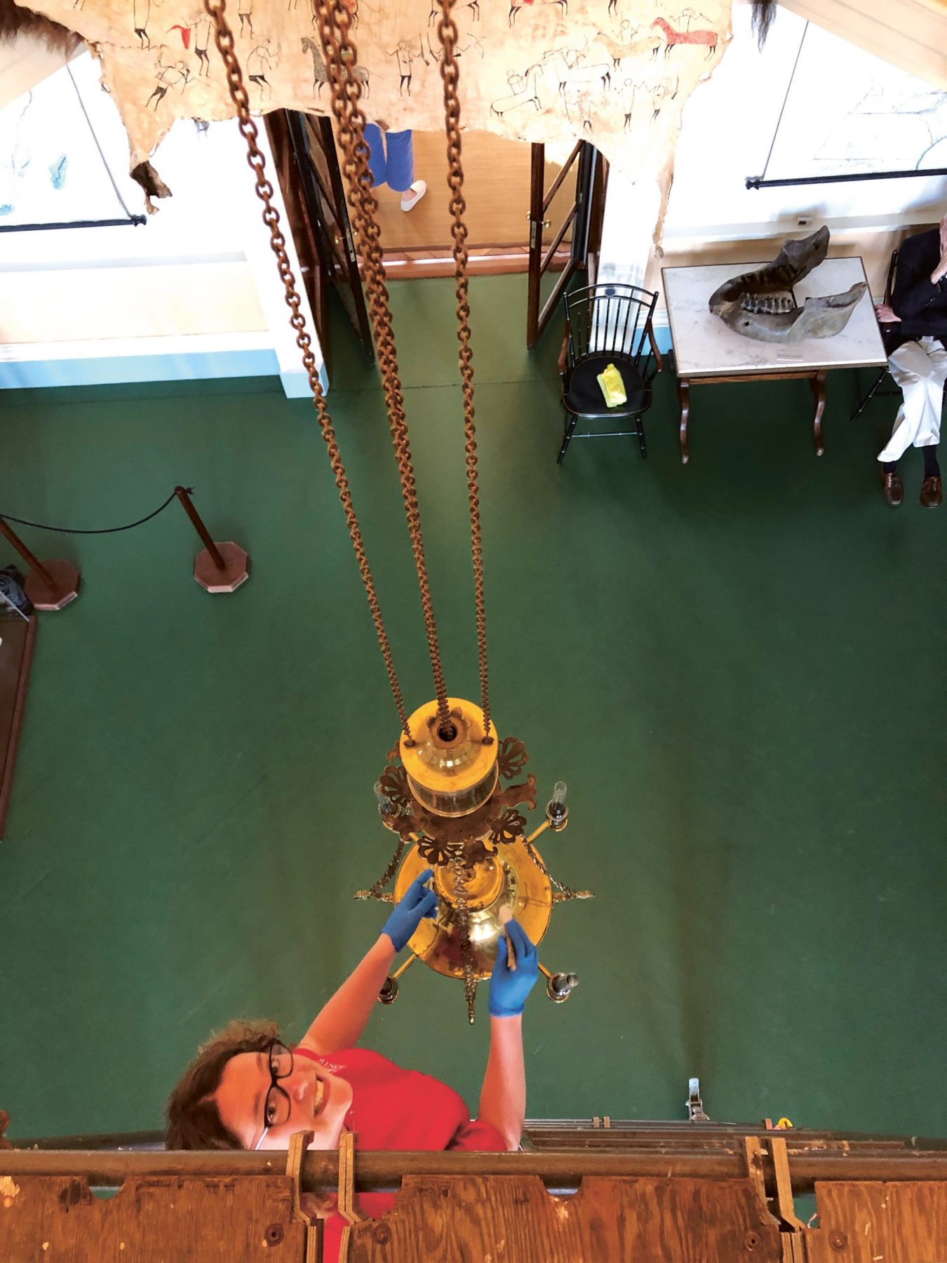 woman cleans a light fixture hanging from the ceiling