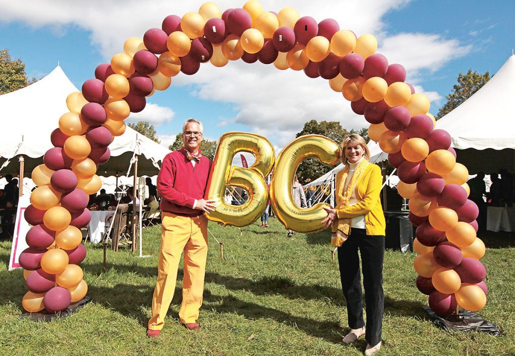 two people stand in the middle of an arch made of balloons holding gold B and C balloons