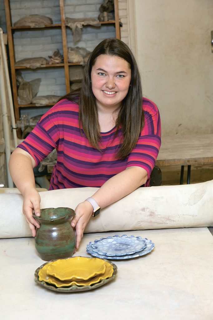 Young woman sits behind pottery