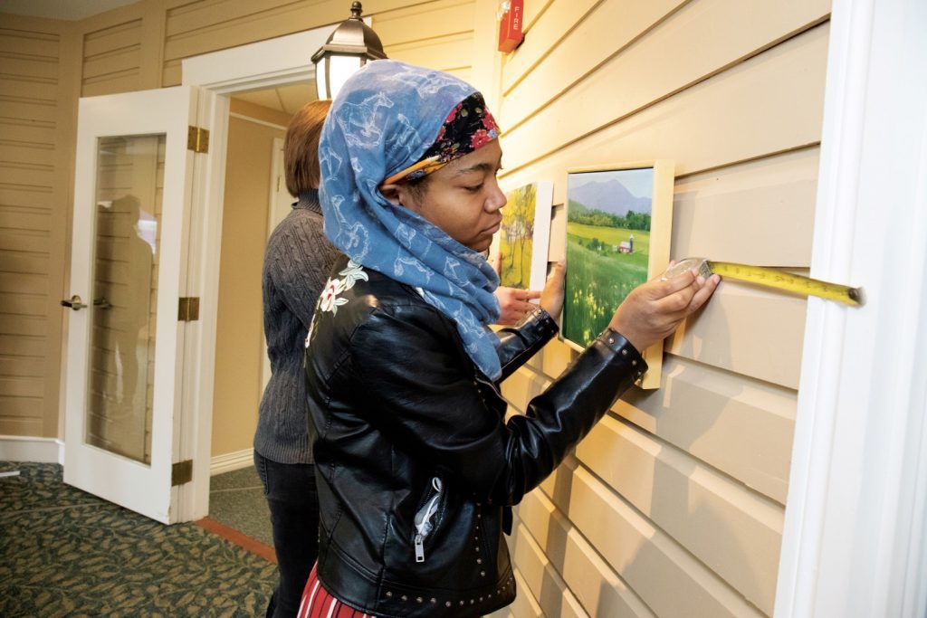 Young woman hangs a painting on a wall with a tape measure