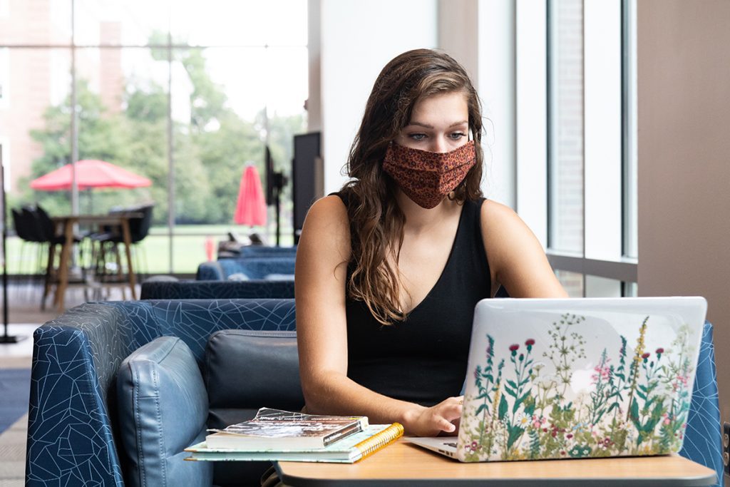 Young lady wearing a mask sits in front of a laptop