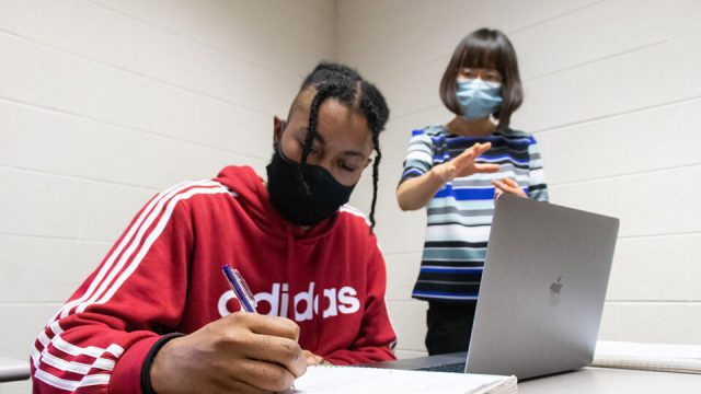 Student writing on a notebook in the background who are both wearing masks