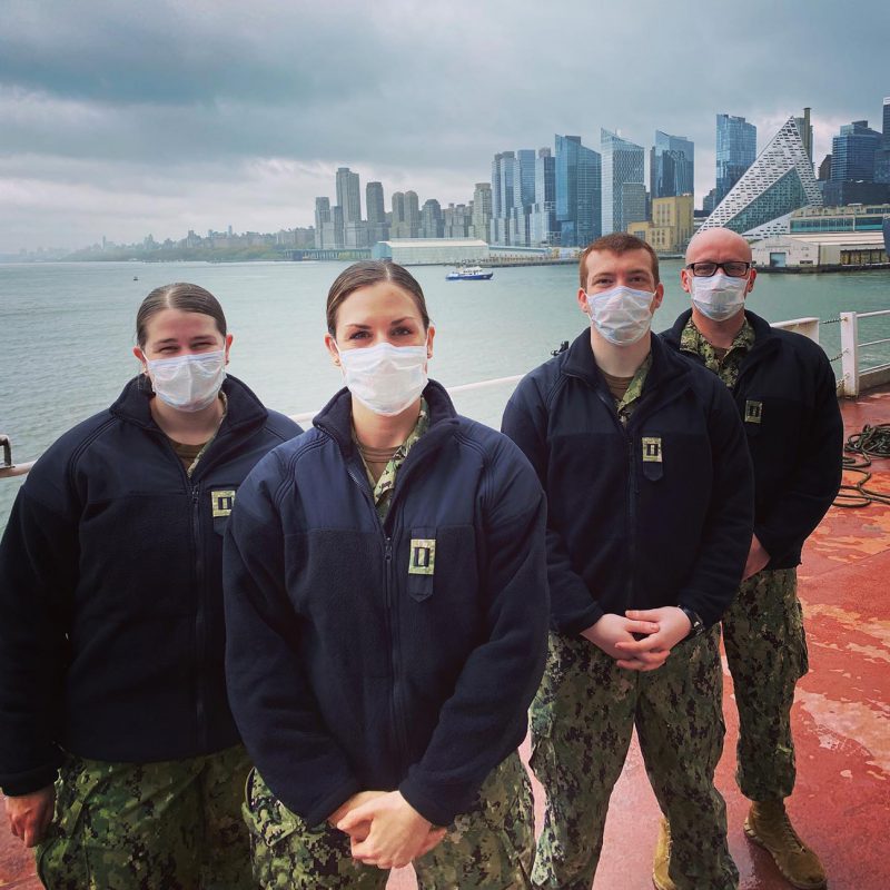 Four people stand on a dock wearing face masks