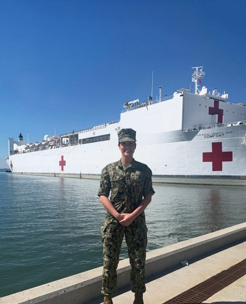 Woman in Navy fatigues stands in front of U.S. Naval hospital ship Comfort