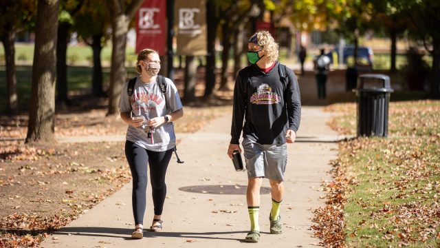A female and male student walk on Bridewater's campus wearing masks