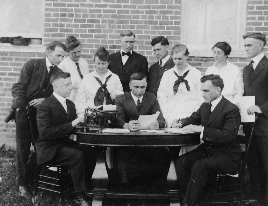 group of people sit around a table with a typewriter and papers