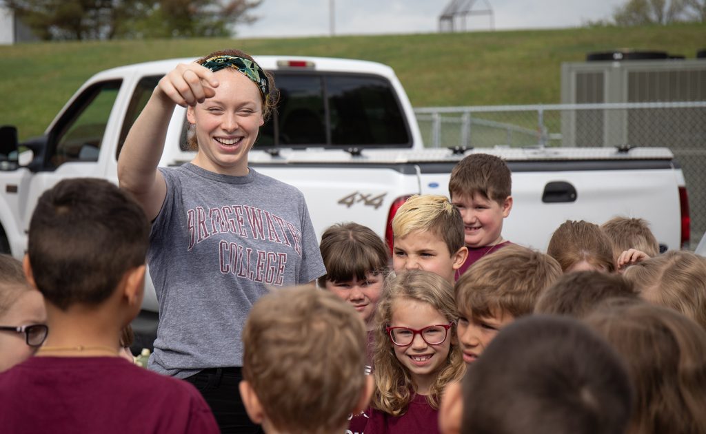 Female with a grey Bridgewater College tshirt speaking to a group of children