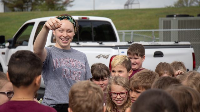 Female with a grey Bridgewater College tshirt speaking to a group of children