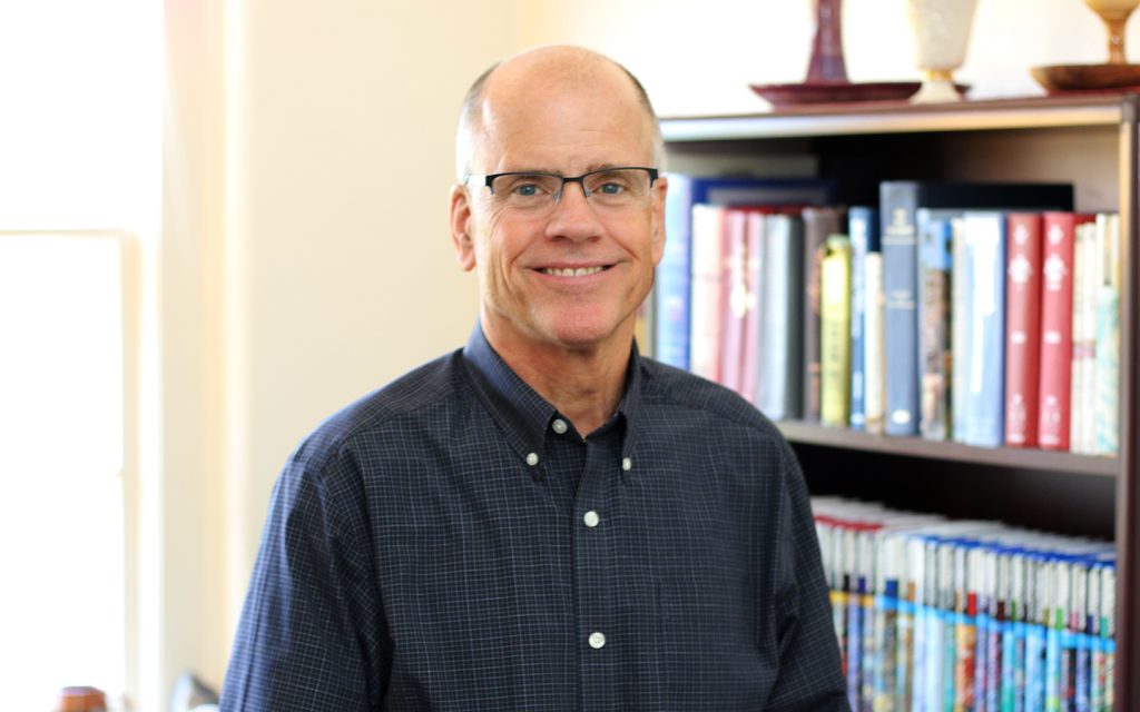 Portrait of Chaplain, Robbie Miller with books in the background