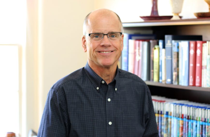 Portrait of Chaplain, Robbie Miller with books in the background