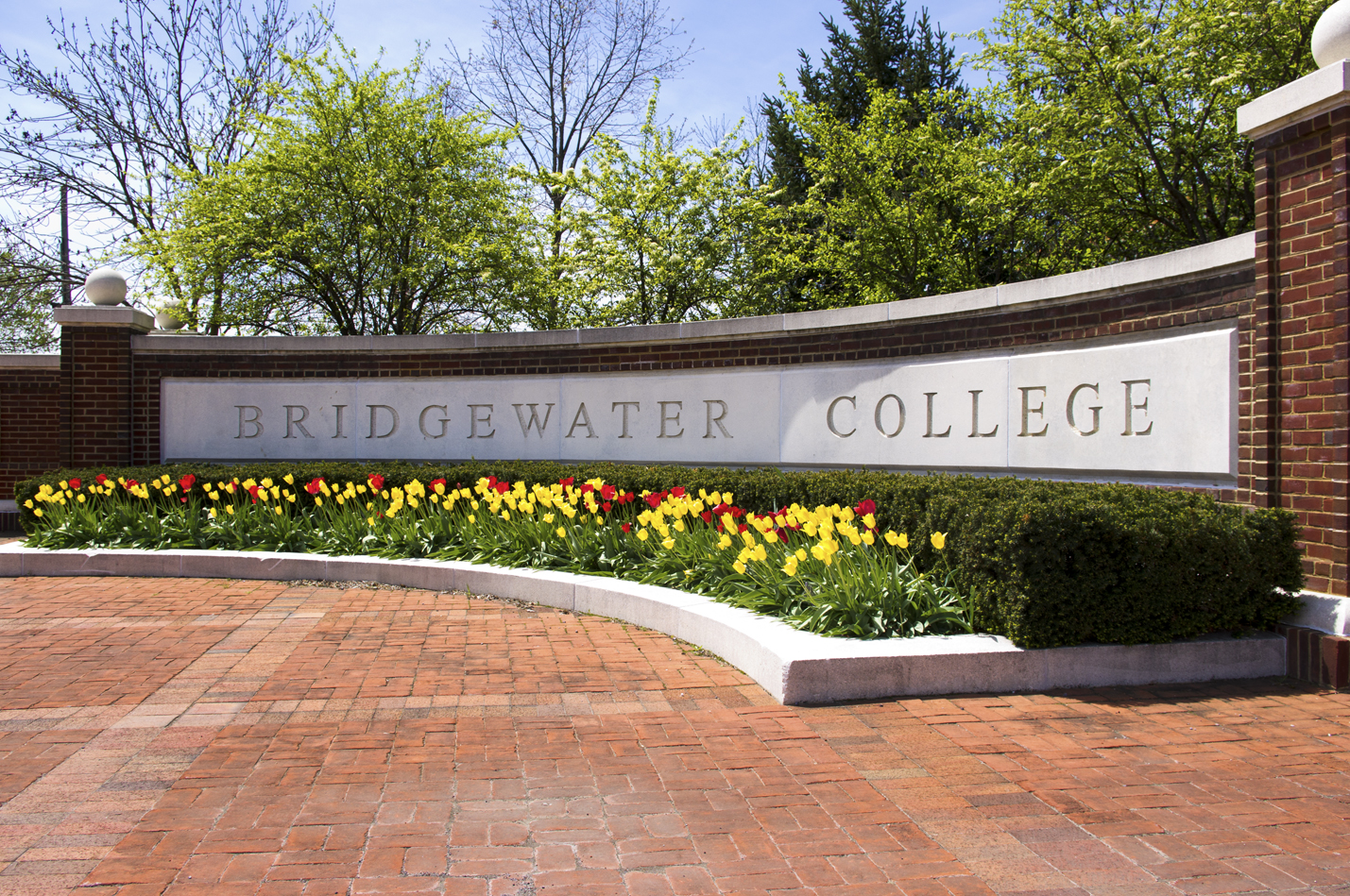 The Bridgewater College cornerstone with red and yellow flowers blooming in front of it