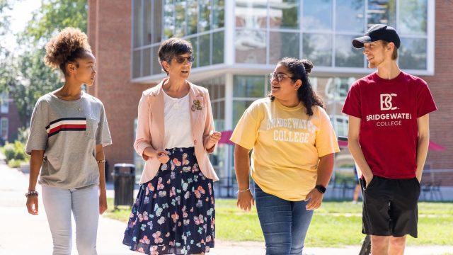 3 students walk alongside a professor on a sunny day