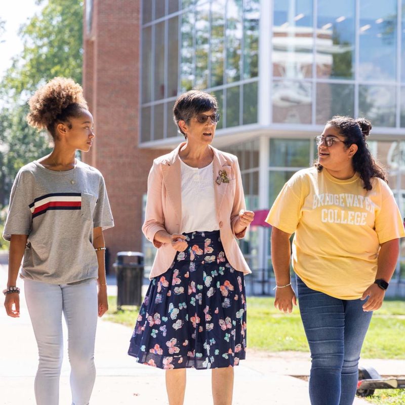 3 students walk alongside a professor on a sunny day