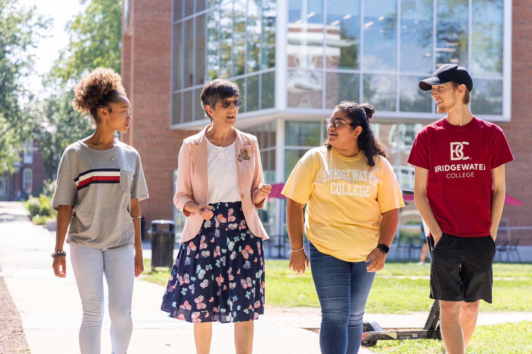 3 students walk alongside a professor on a sunny day