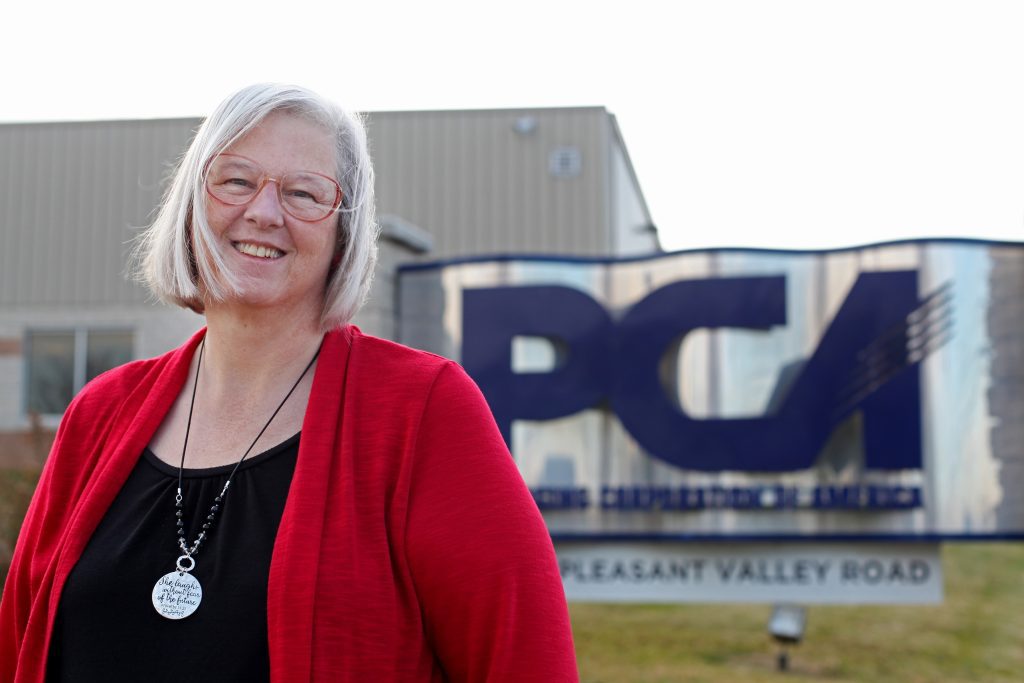 Denise Massie M'22 stands in front of a sign for Packaging Corp of America where she works in Harrisonburg, Virginia. The sign reads P-C-A.