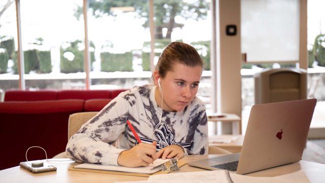 Student writing on a piece of paper while looking at laptop