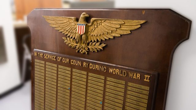 A large wooden board with a gold Eagle on top and the words "In Service of our country during World War II." A list of names is shown underneath