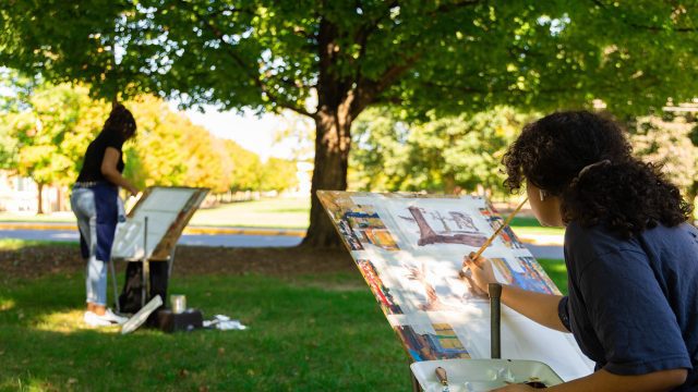 Two students painting artwork outside