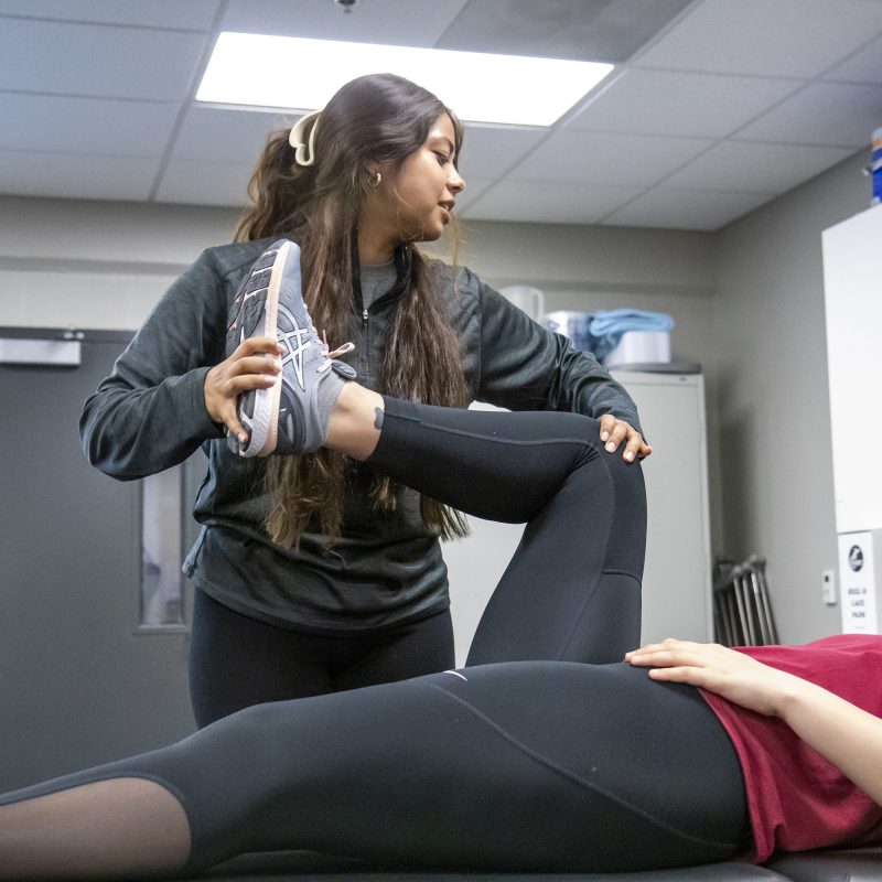 Female student helping student stretch in athletic training class
