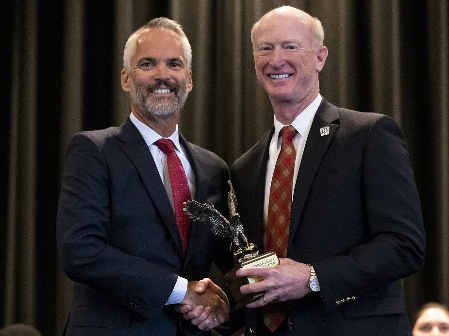 Two men shake hands while being presented an award on stage