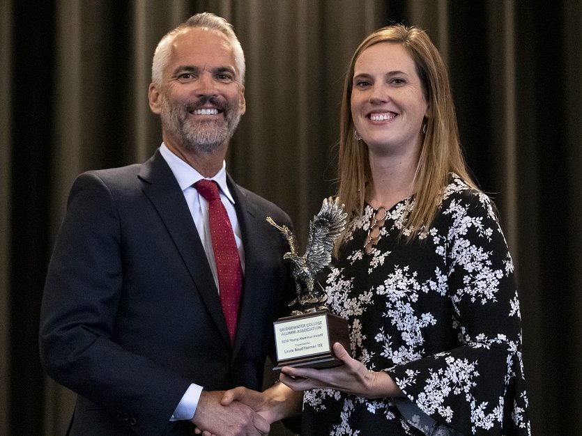 A man and a woman shake hands while being presented an award on stage