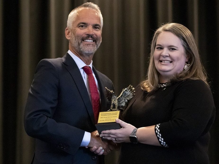 A man and a woman shake hands while being presented an award on stage