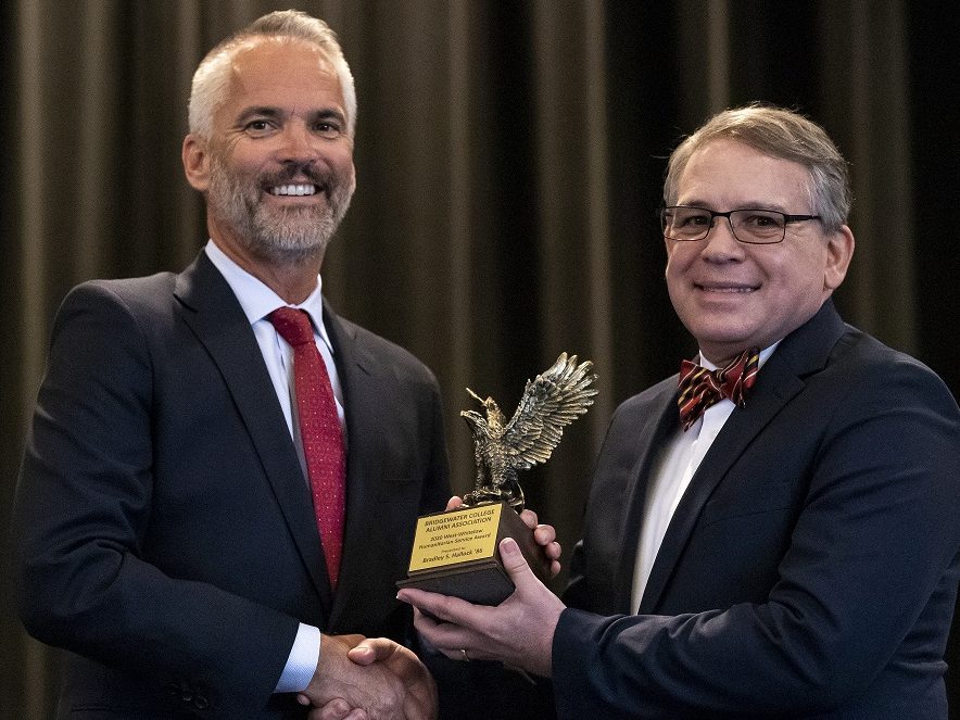 Two men shake hands while being presented an award on stage