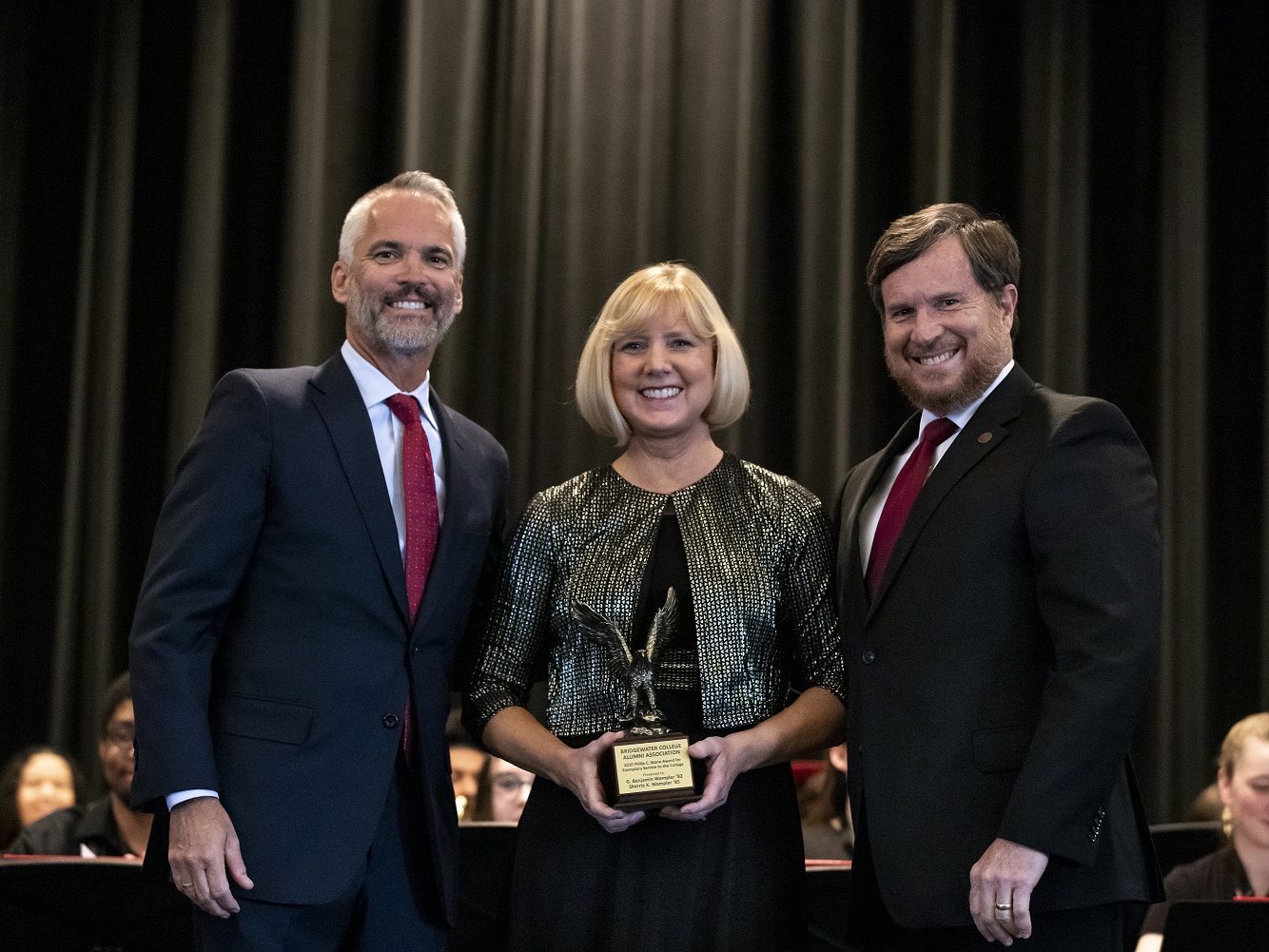 Two men and a woman pose on stage with an award