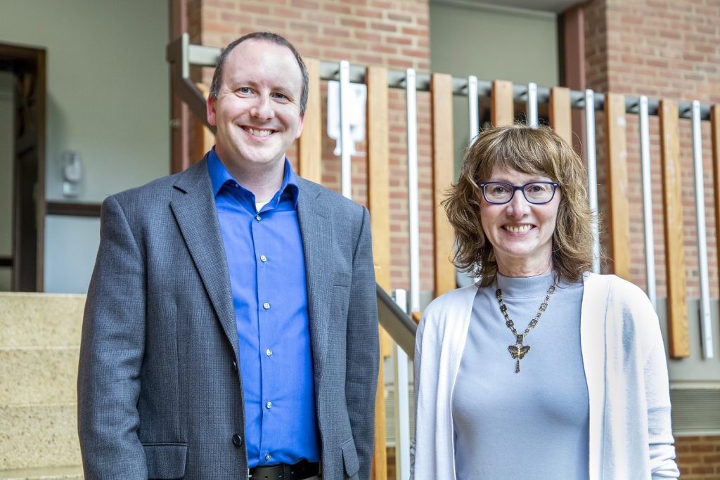 A man and woman stand side-by-side smiling on a staircase