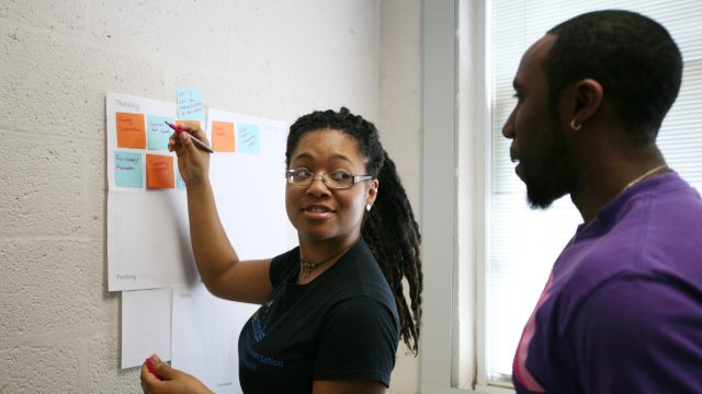 Student putting post it notes on wall while talking to another student