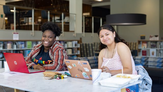 Two students sitting at a desk working and smiling for the camera