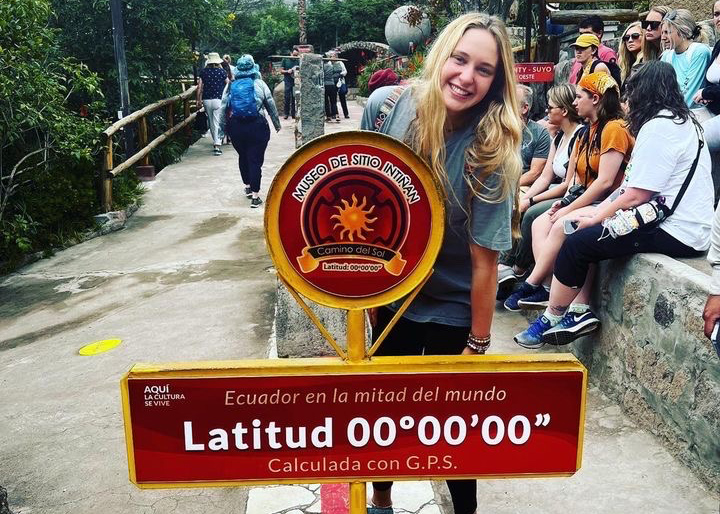 Female student standing in front of latitude sign in Ecuador