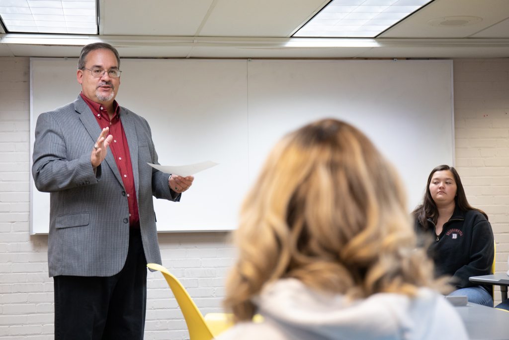 Professor standing at the front of the room talking to student