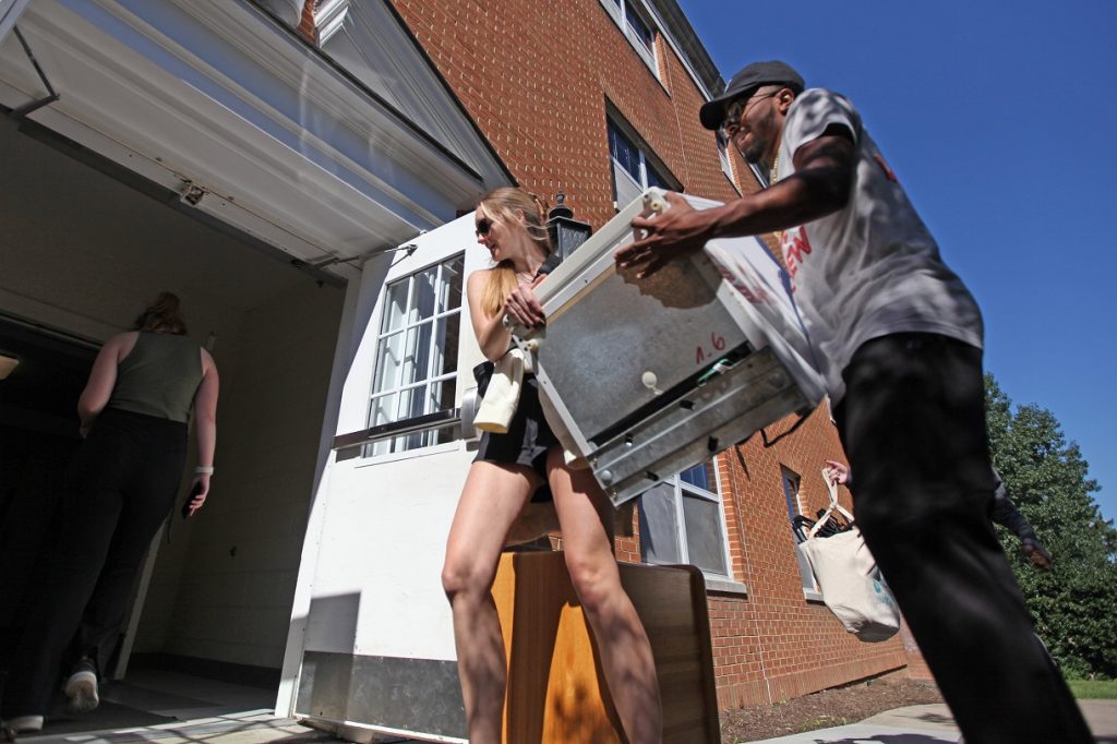 a female and male student carrying a mini fridge into a dorm room on move in day