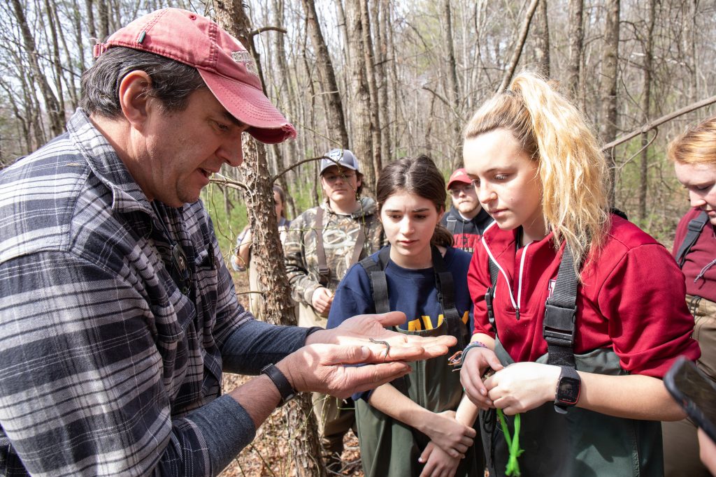 Professor holding creature in his hands while students observe. 