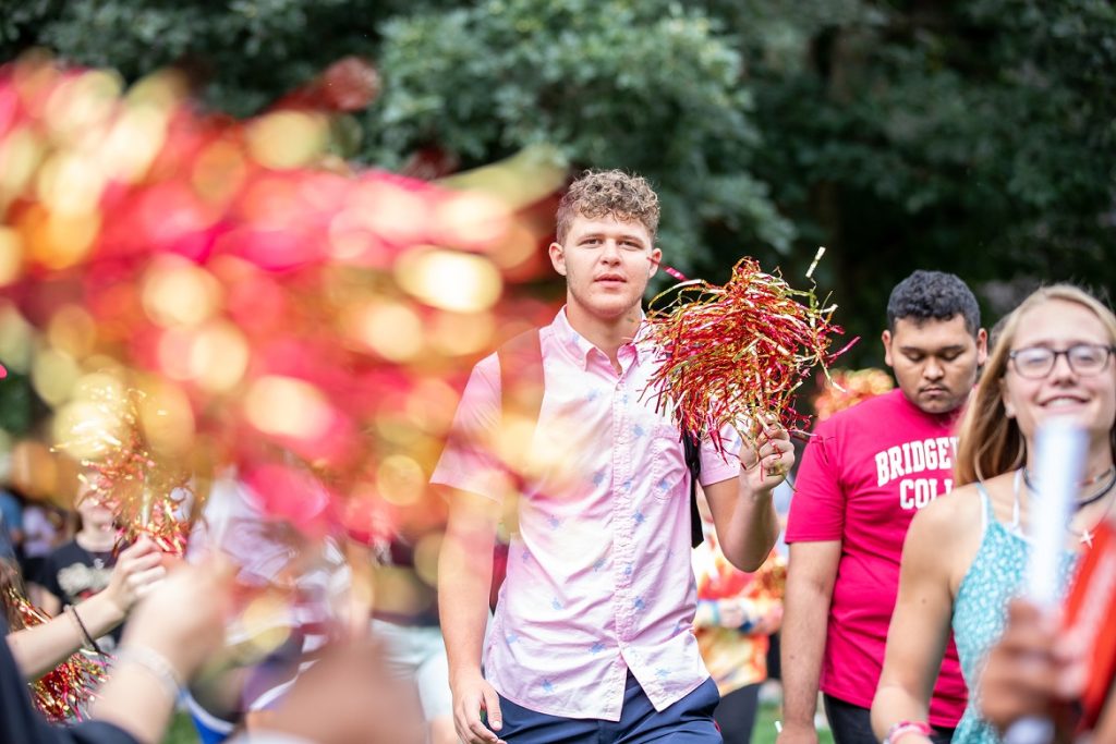 a male student walks through a row of people waving crimson and gold pompoms