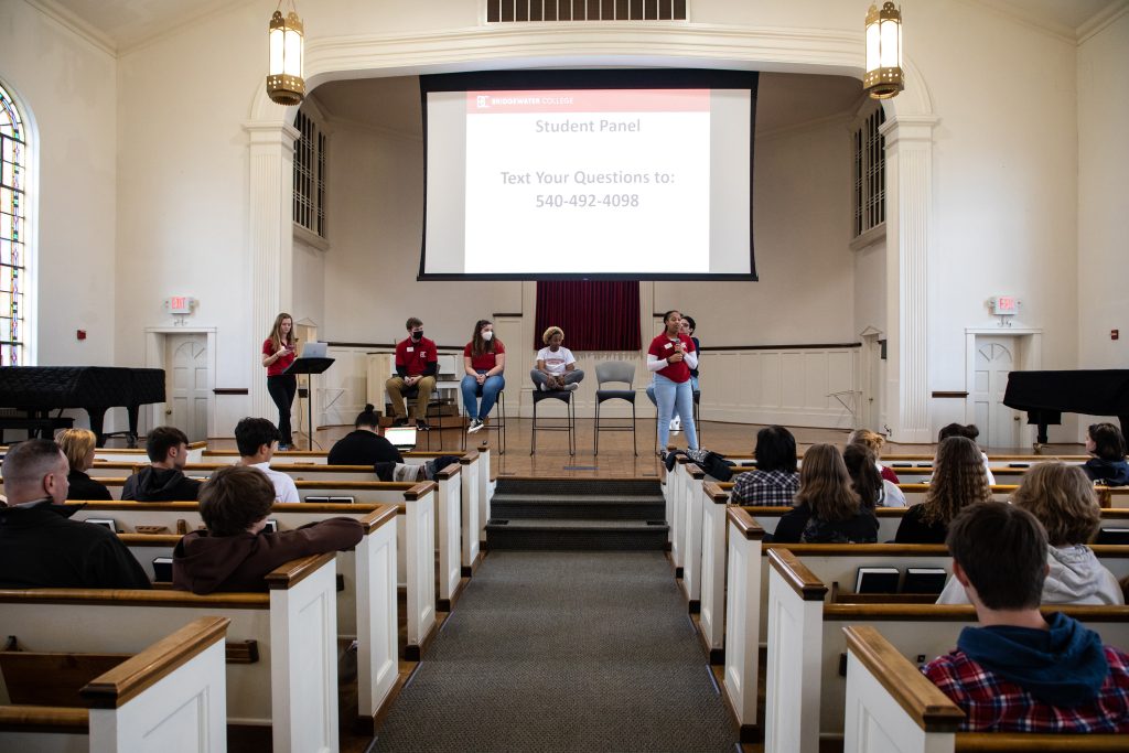 Student panel standing on stage with projector screen behind them