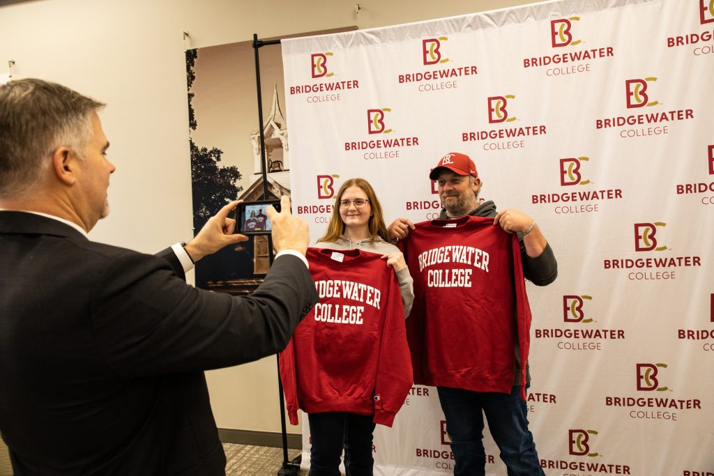 Father and daughter holding up Bridgewater College sweatshirts while someone takes a picture