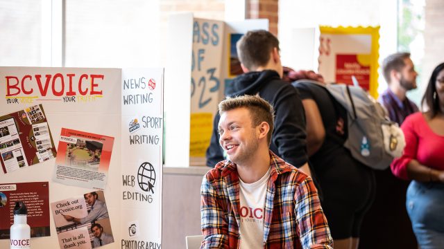 Student sitting in front of poster at club/org fair