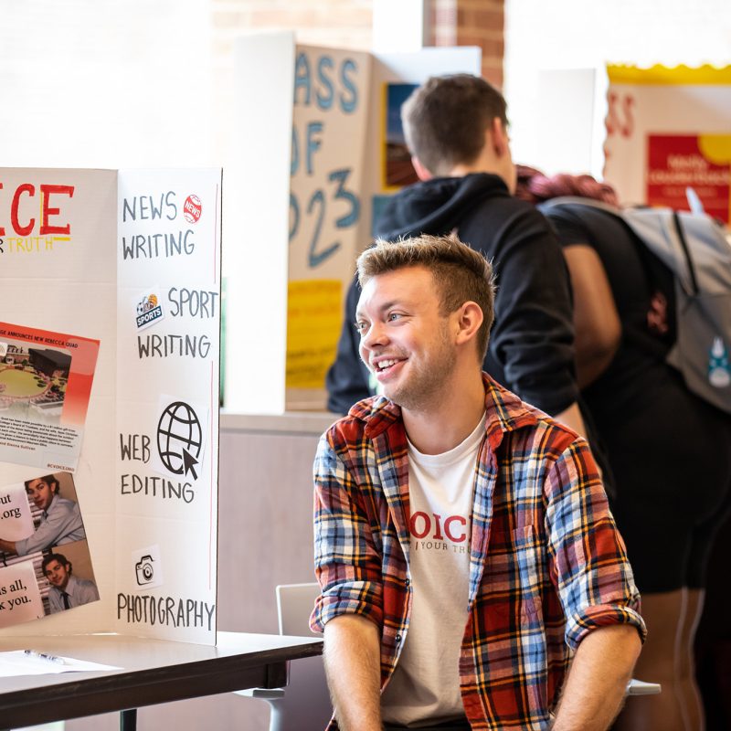 Student sitting in front of poster at club/org fair