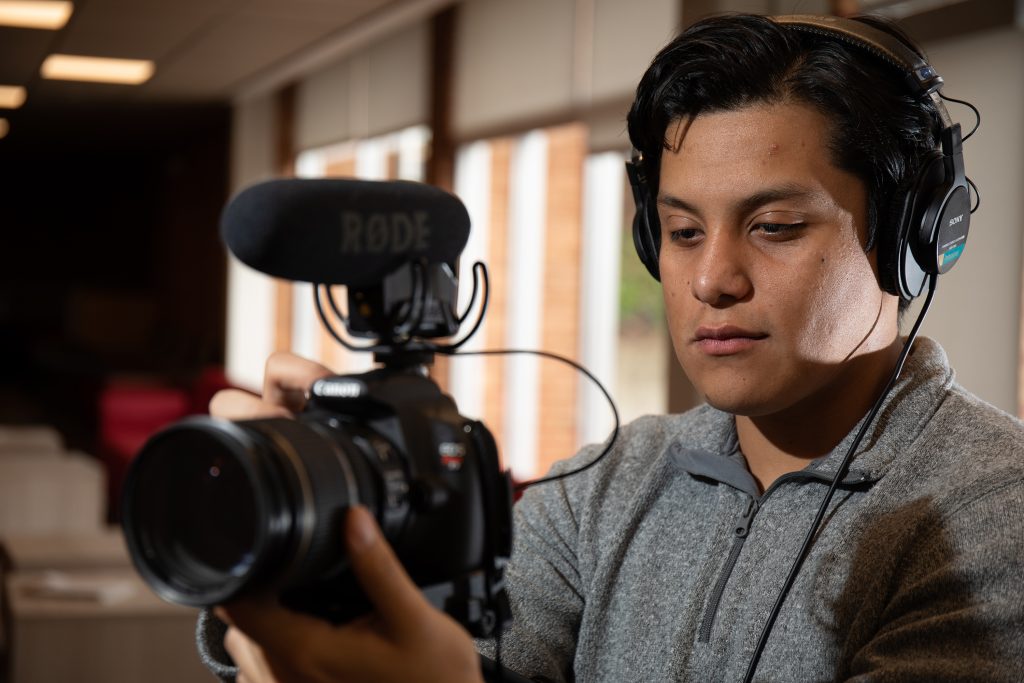 Student with headphones holding camera with microphone 