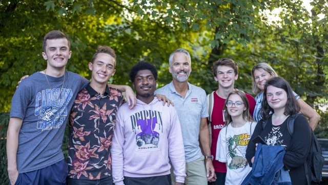 Six students pose for a photo outside with Bridgewater College President David Bushman and his wife, Suzanne. All are smiling.