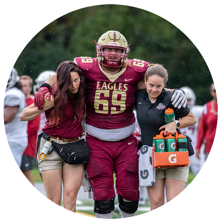 Two athletic trainers helping football player off the field